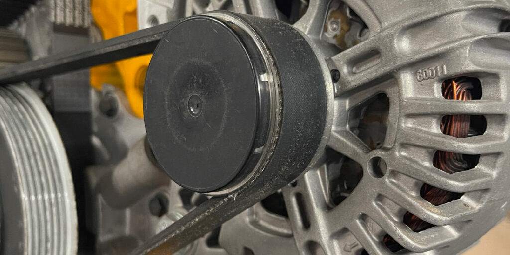 Close-up of cracked serpentine belt edge lines in car engine showing deep fissures on rubber ribs
